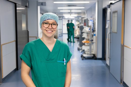 Lächelnde Pflegekraft im Krankenhausflur, trägt grüne OP-Kleidung.