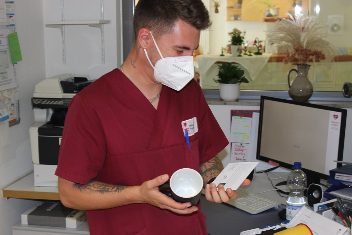 Krankenpfleger in roter Uniform hält Tasse und Karte im Krankenhausbüro.