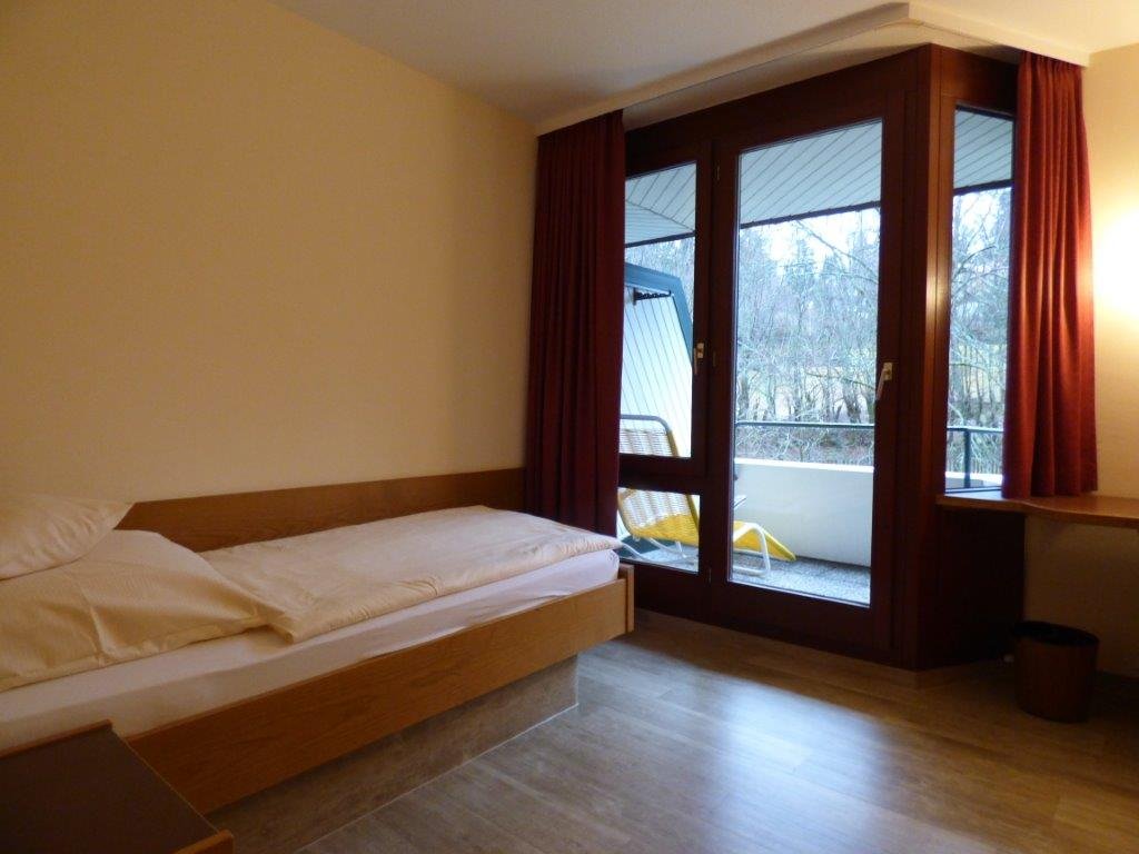 Krankenhaus-Einzelzimmer mit Bett, Schreibtisch und Balkon.