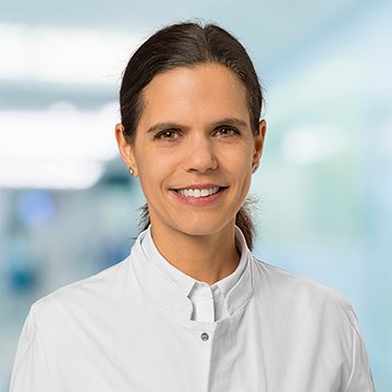 Ärztin in weißem Kittel lächelt im Krankenhausflur.