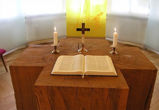 Kirchenaltar mit aufgeschlagener Bibel und zwei brennenden Kerzen.