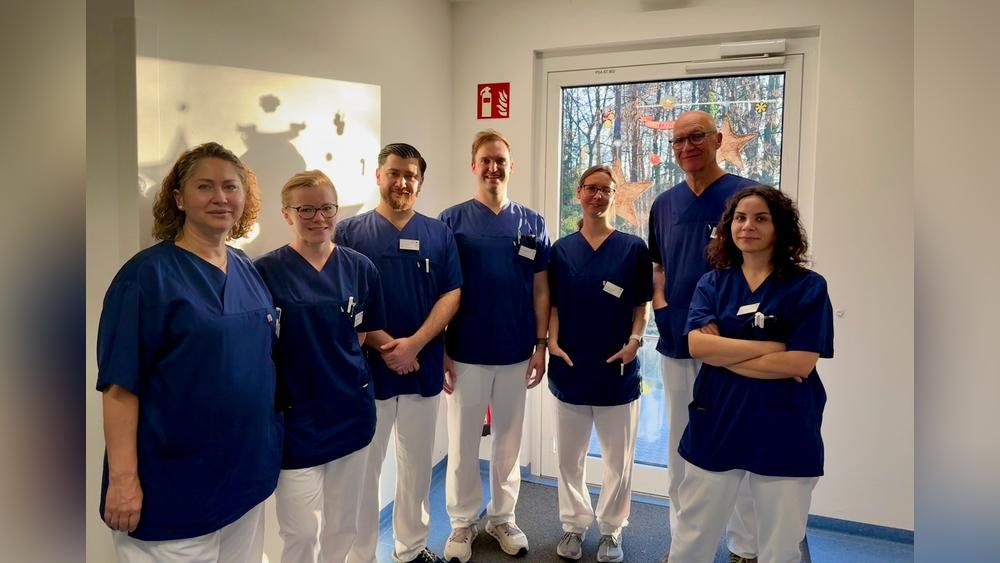 Sieben Krankenhausmitarbeiter in blauen Kitteln lächeln in die Kamera.