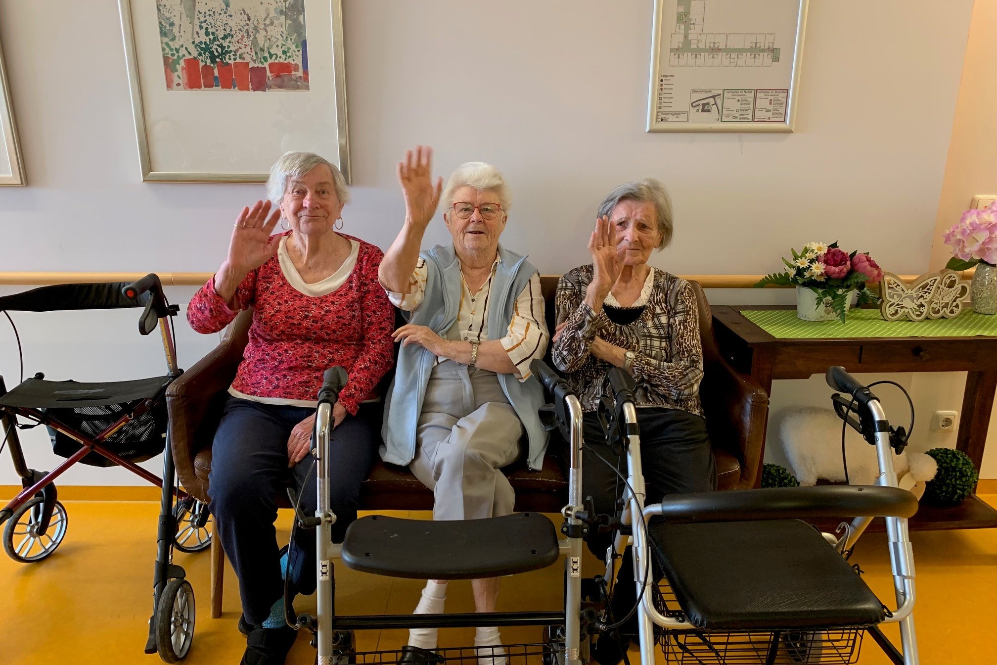 Drei Seniorinnen im Seniorenzentrum Eckental winken, umgeben von Rollatoren.