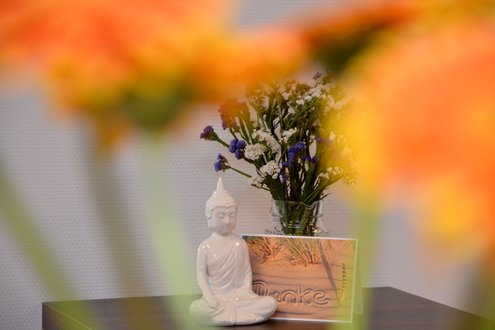 Weiße Buddha-Statue und Blumenstrauß auf Tisch, umgeben von orangefarbenen Blumen.