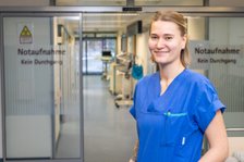 Krankenschwester in blauer Uniform vor Notaufnahme-Tür im Krankenhausflur.