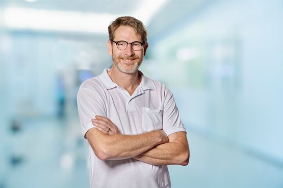 Mann in weißem Hemd steht in hellem Krankenhausflur.