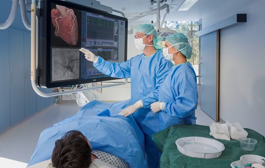 Ärzte im Herzkatheterlabor erklären Koronarangioplastie an einem Monitor.
