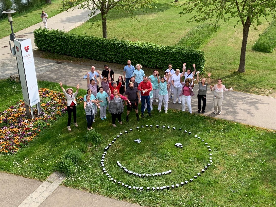 Gruppe von Menschen feiert lächelnd im Park neben einem Smiley aus Kerzen.