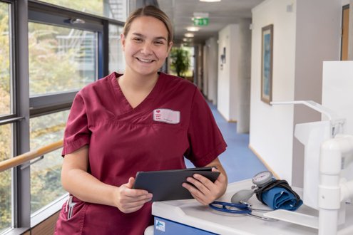 Pflegemitarbeiterin in roter Uniform mit Tablet im Krankenhausflur.