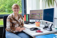 Lächelnde Frau am Schreibtisch mit Computermonitoren und Bürobedarf.