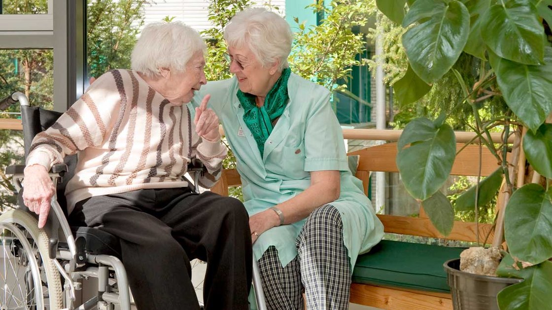 Pflegerin unterhält sich mit Seniorin im Rollstuhl im Seniorenzentrum Nürnberg.