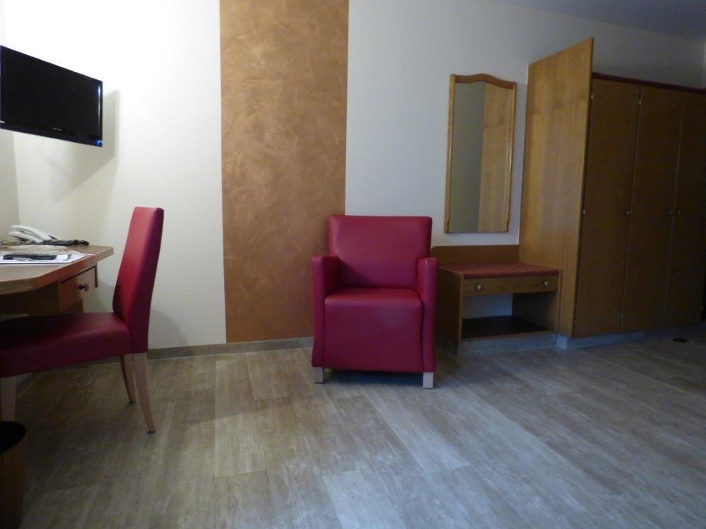Krankenhauszimmer mit rotem Sessel, Schreibtisch und Fernseher.