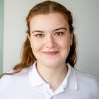 Porträt einer lächelnden Frau in weißem Hemd vor neutralem Hintergrund.
