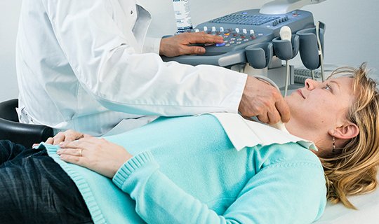 Ärztliche Ultraschalluntersuchung am Hals einer Patientin in medizinischer Umgebung.