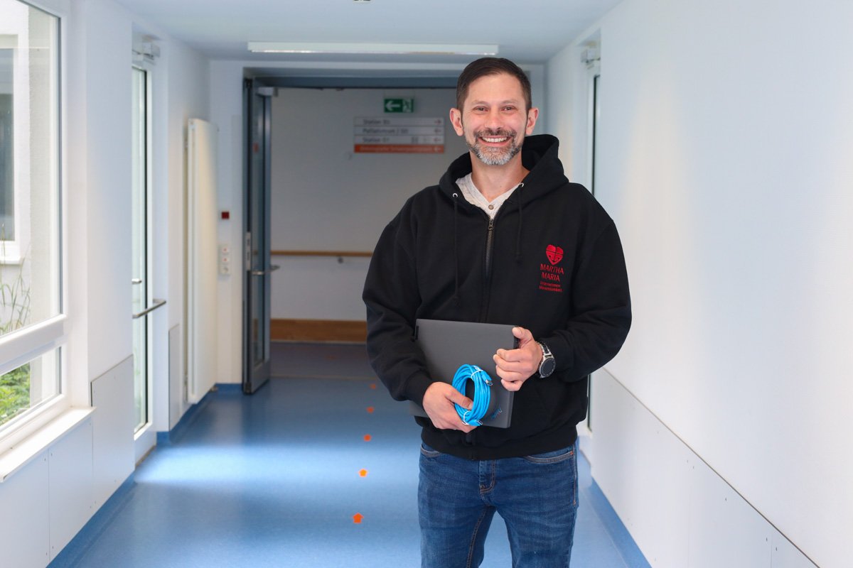 Mann im Flur des Krankenhauses Martha-Maria, hält Laptop und Kabel.