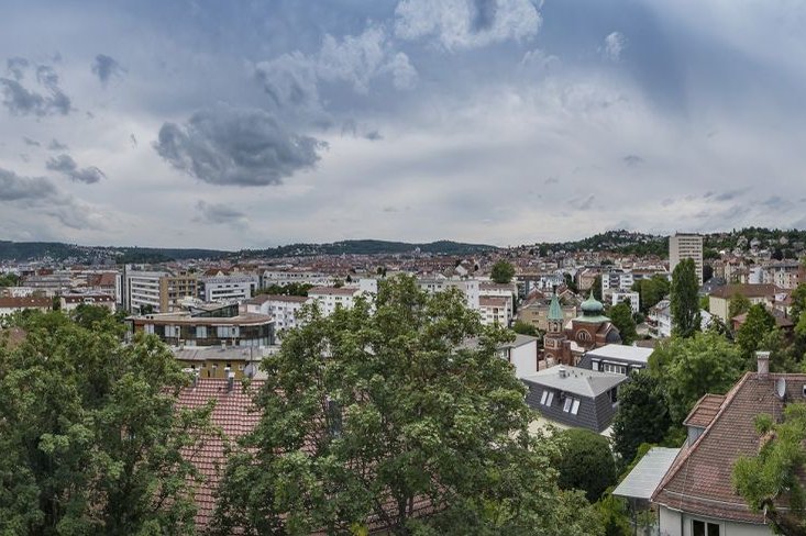 Panoramablick auf Stuttgart mit grüner Vegetation im Vordergrund, bewölkter Himmel.