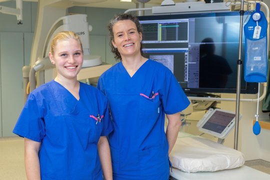 Zwei lächelnde Pflegekräfte in blauer Uniform im Krankenhaus.