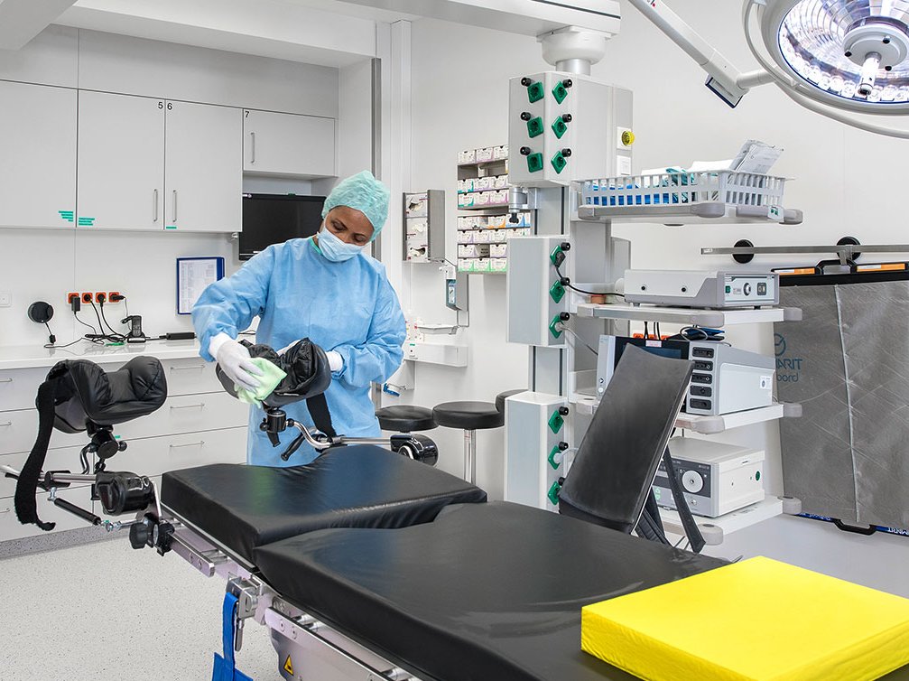 Mitarbeiterin reinigt Operationssaal mit Desinfektionstuch, um Hygiene sicherzustellen.