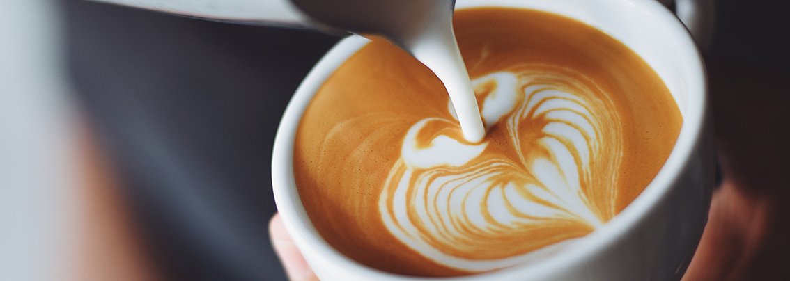 Barista gießt Milch in Cappuccino mit Latte Art im Krankenhaus-Bistro.