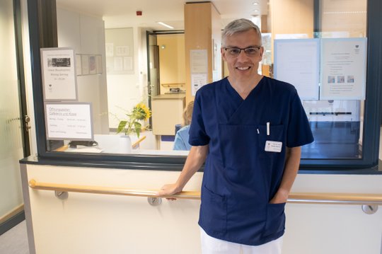 Chefarzt in blauer Uniform vor der Rezeption der Klinik in München.