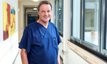 Arzt in blauer OP-Kleidung lächelt im Krankenhausflur der Klinik.