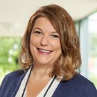Lächelnde Frau mit braunen Haaren vor verschwommenem Hintergrund.