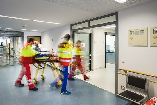 Rettungskräfte bringen Patienten auf Trage in Krankenhausflur.