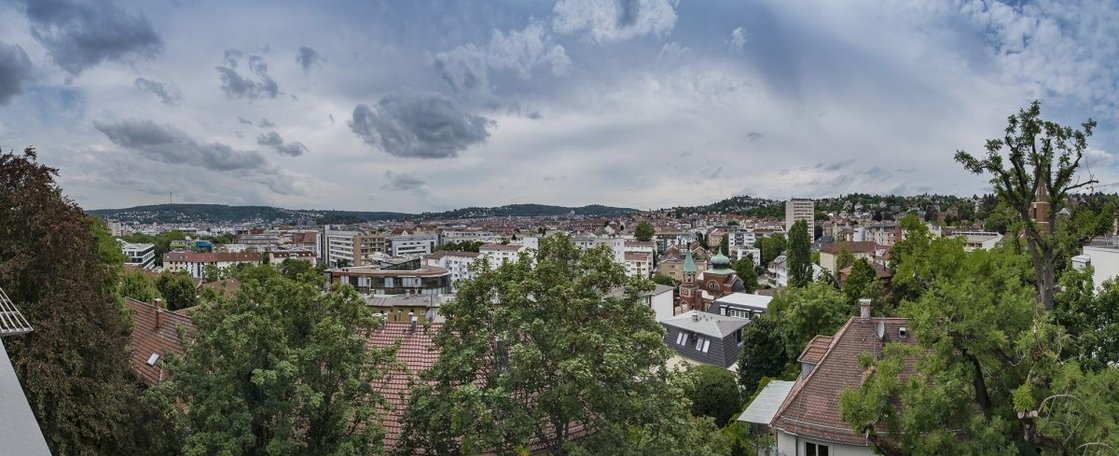 Panoramablick auf Stuttgart mit grüner Vegetation im Vordergrund, bewölkter Himmel.