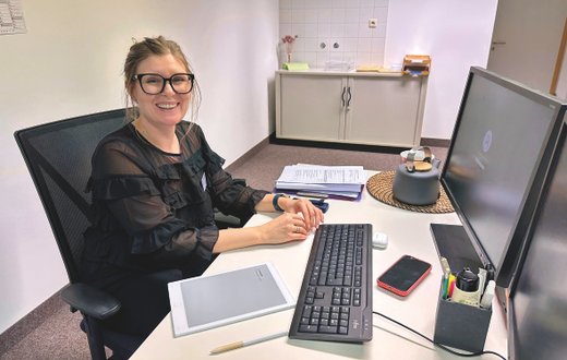 Lächelnde Frau am Schreibtisch mit Computer, Stift und Notizblock.