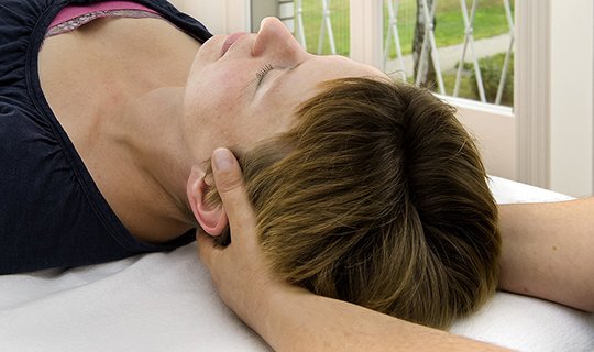 Therapeut hält Kopf eines liegenden Patienten in Einzeltherapie-Sitzung.