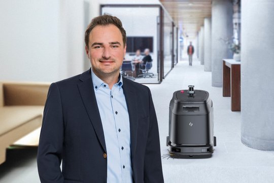 Mann in Büroflur neben einem Reinigungsroboter, symbolisiert innovative Arbeitsumgebung.