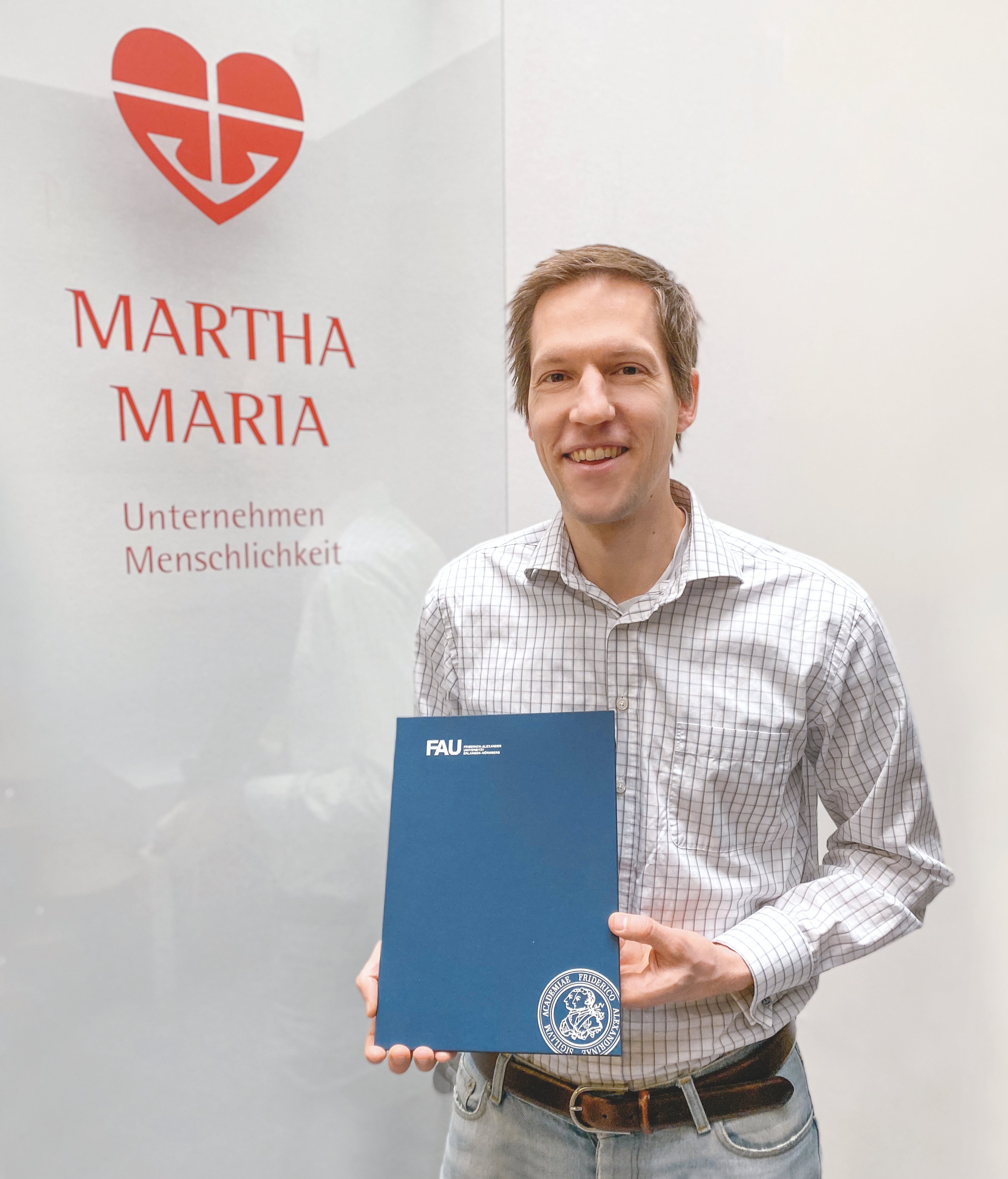 Mann hält FAU-Zertifikat vor Martha Maria Logo.