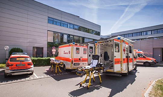 Krankenwagen vor Krankenhausgebäude mit geöffneten Türen und Tragen.