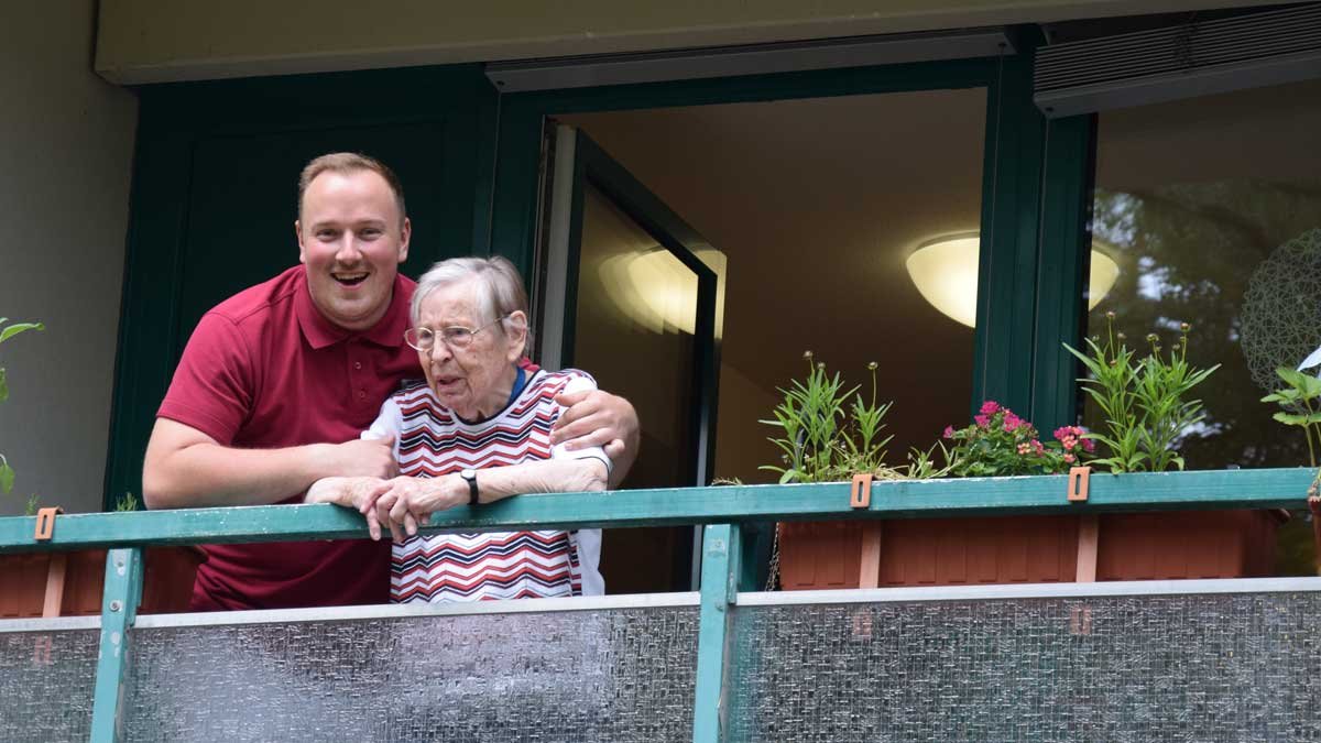 Pfleger unterstützt Seniorin auf dem Balkon im Seniorenzentrum Nürnberg.