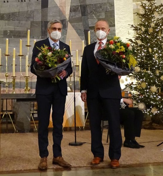Zwei Männer mit Blumensträußen stehen vor Altar und Weihnachtsbaum.