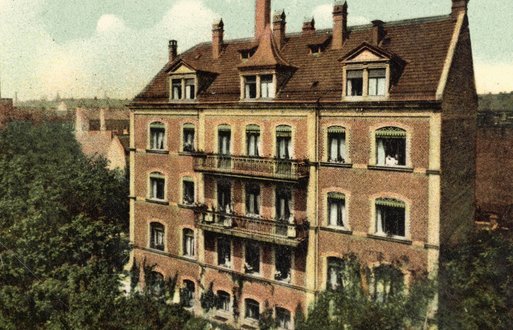 Historisches Krankenhausgebäude umgeben von Bäumen, mit roten Ziegelmauern und vielen Fenstern.