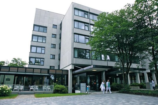 Krankenhausgebäude mit Bäumen und Ärzten im Vordergrund.