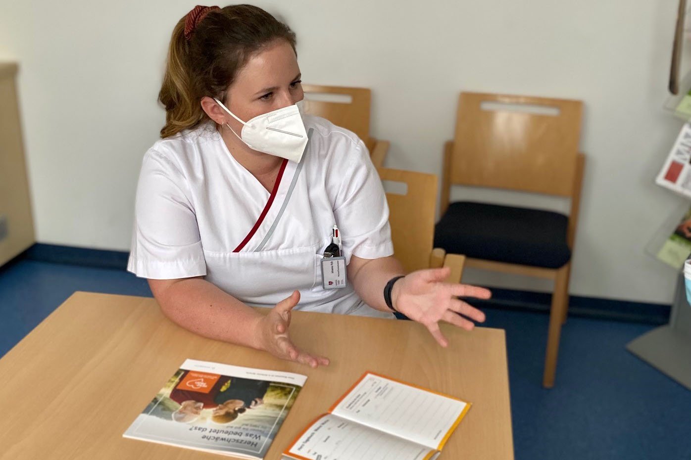 Pflegekraft im Gespräch, hält Broschüre und Notizbuch auf Tisch.