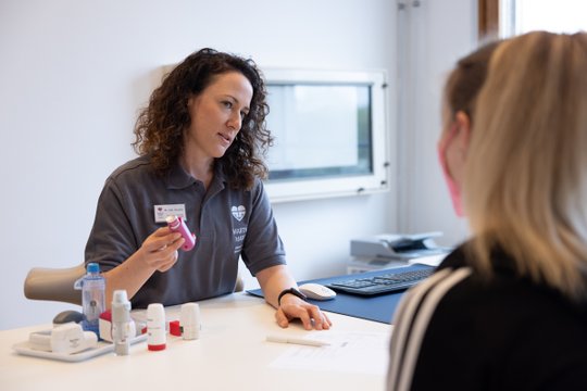 Ärztin erklärt Patientin den Gebrauch eines Asthma-Inhalators in Klinik.