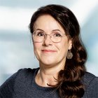 Porträt einer lächelnden Frau mit Brille und langen, dunklen Haaren.