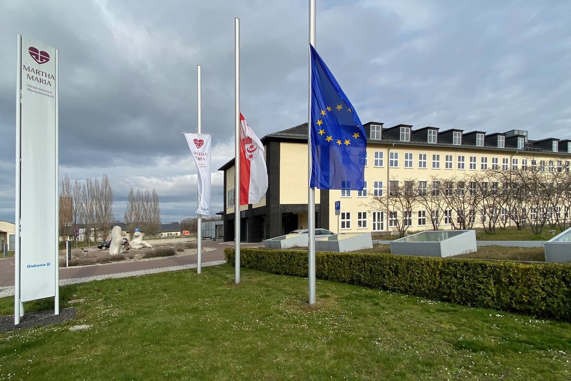 Gebäude mit Martha-Maria-Logo und europäischer Flagge vor bewölktem Himmel.