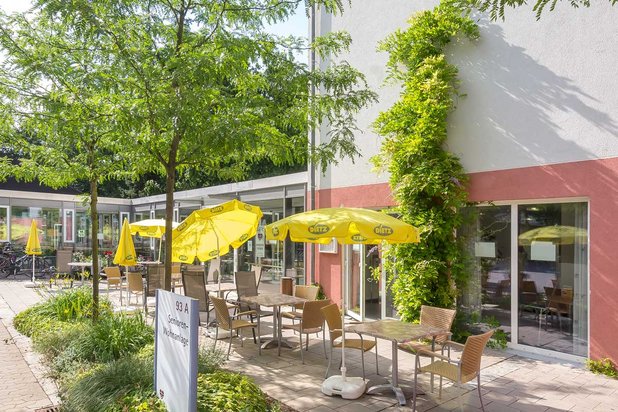 Terrasse des Seniorenzentrums Nürnberg mit gelben Sonnenschirmen und Tischen.