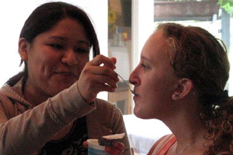 Zwei Frauen, eine füttert die andere mit einem Löffel.