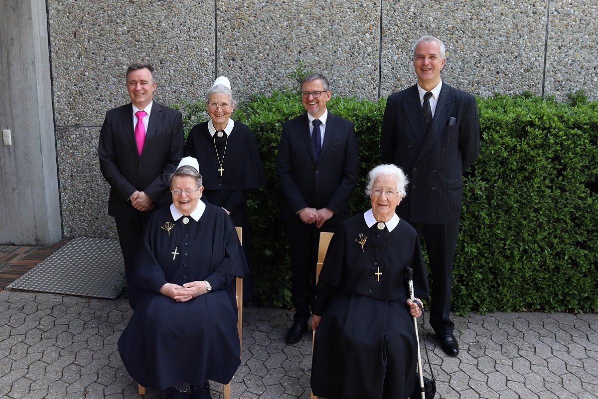 Feierliche Gruppenfoto von Nonnen und Männern vor einer Wand mit Pflanzen.