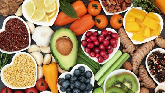 Gesunde Lebensmittel wie Avocado, Beeren und Paprika auf einem Tisch arrangiert.