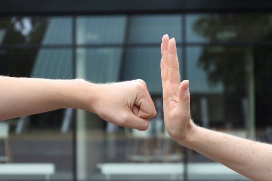Zwei Hände in symbolischer Geste, Faust und Handfläche, vor Glasgebäude.