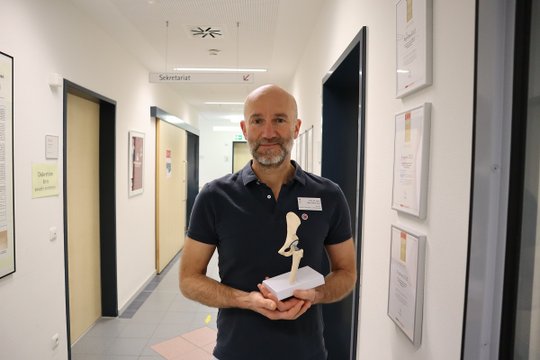 Arzt im Krankenhausflur hält ein Modell einer Hüftprothese.