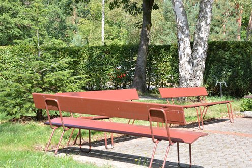 Rote Bänke im sonnigen Klinikgarten, umgeben von Bäumen und Hecken.