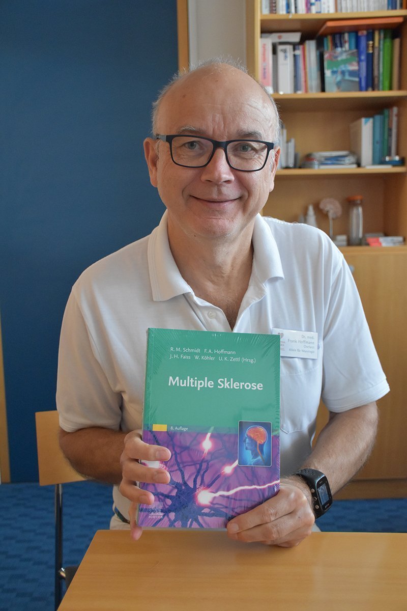 Mann hält ein Buch über Multiple Sklerose in einem Büro.