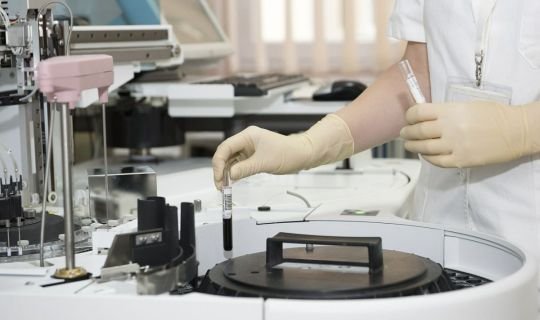 Laborarbeiterin platziert Probenröhrchen in medizinisches Analysegerät.